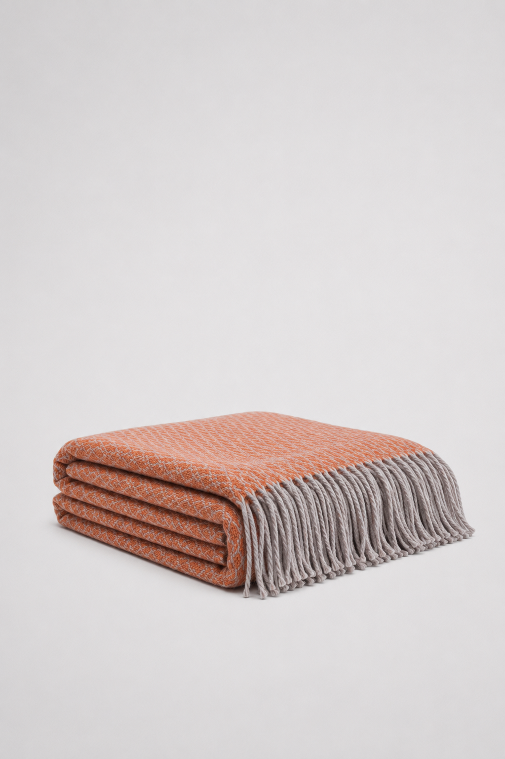 A terracotta orange  and grey soft woven knit throw blanket with a textured diamond pattern and fringe - reversible