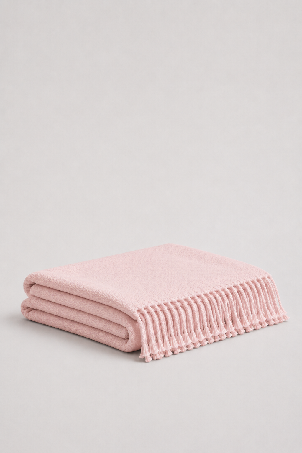A dusty pink soft wool knit throw blanket with fringed edges