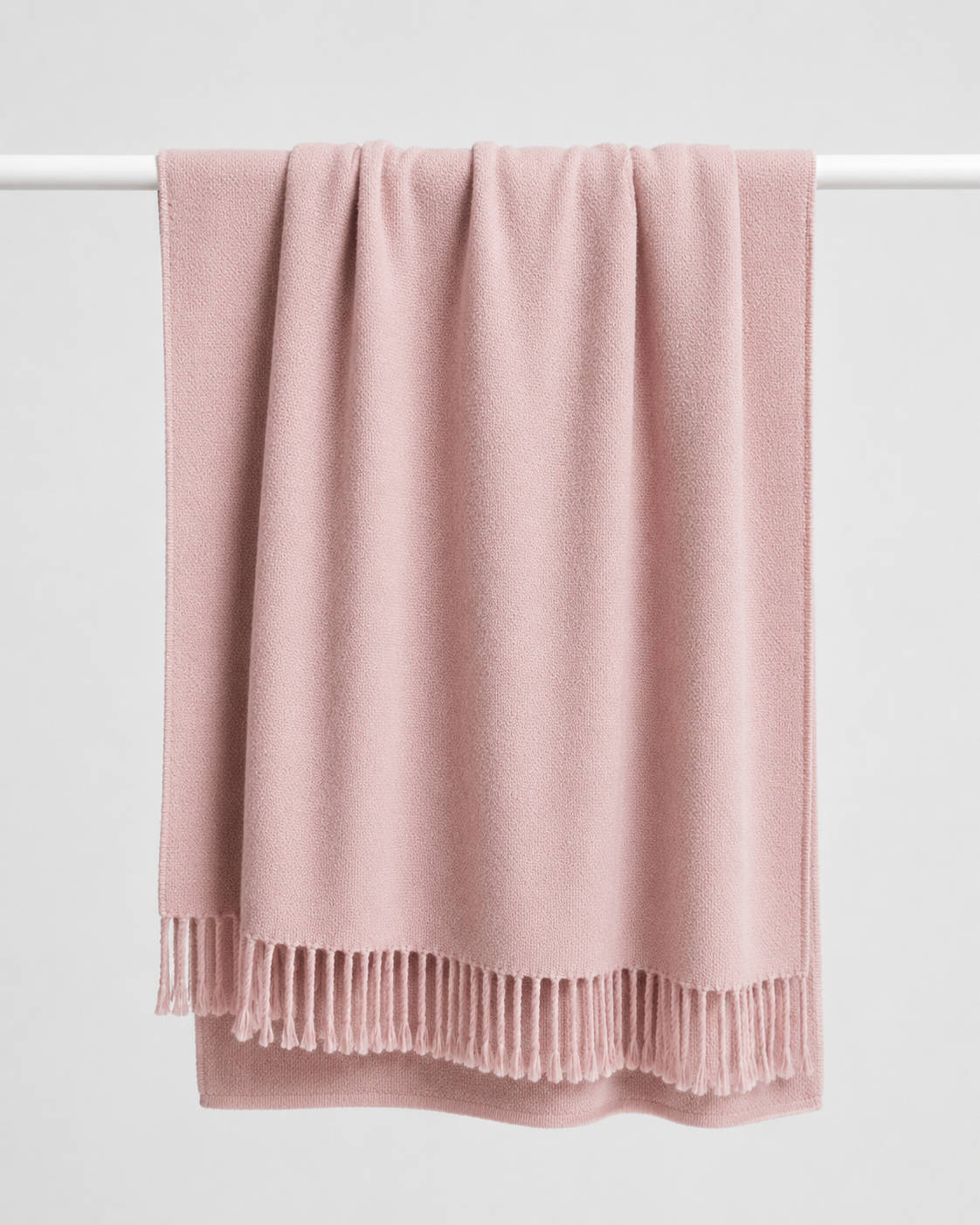 A dusty pink soft wool knit throw blanket with fringed edges