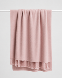 A dusty pink soft wool knit throw blanket with fringed edges