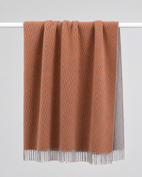 A terracotta orange  and grey soft woven knit throw blanket with a textured diamond pattern and fringe - reversible