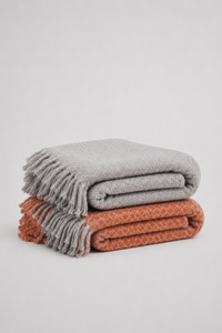 A terracotta orange  and grey soft woven knit throw blanket with a textured diamond pattern and fringe - reversible